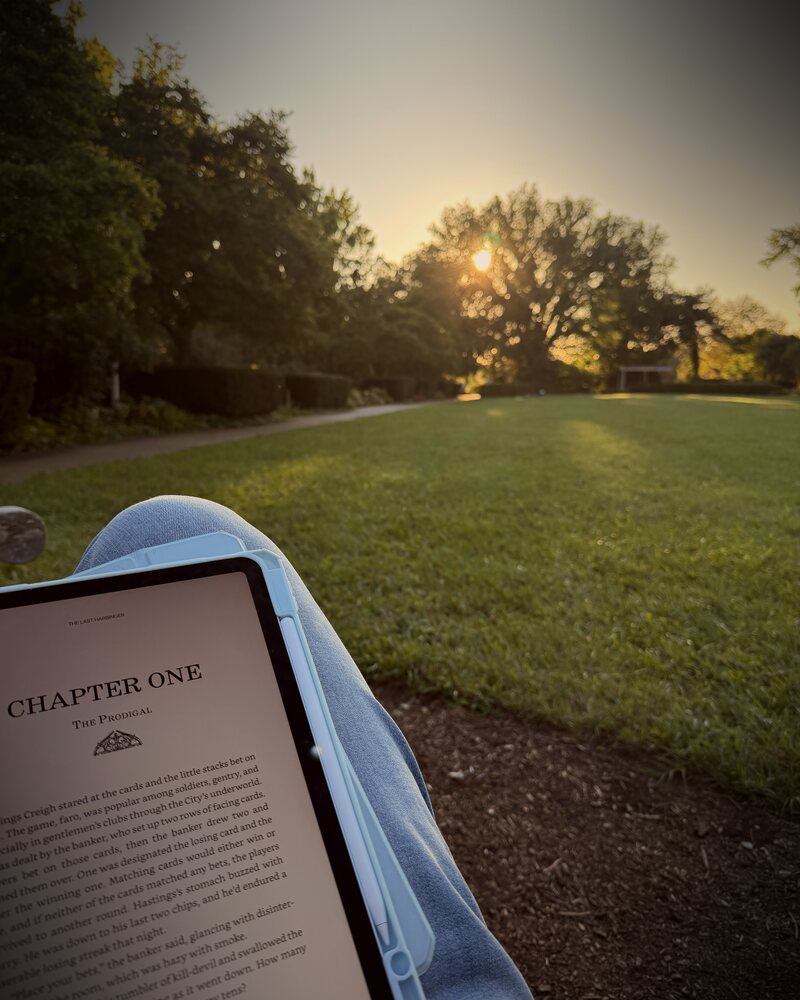 View from the hammock at sunset: an iPad open to chapter one over the Ault Park lawn